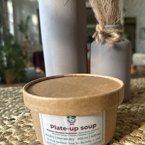 This image is of a brown paper tub with A bone broth based soup for dogs with broccoli, beets, Spinach and healing spices.