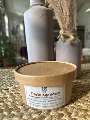 This image is of a brown paper tub with A bone broth based soup for dogs with broccoli, beets, Spinach and healing spices.